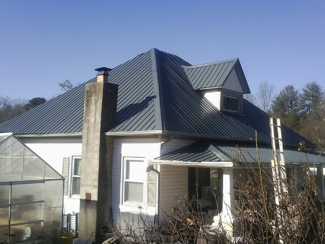 Dark blue standing seam metal roof on a white farmhouse with dormer — Slate & Tile Roof Repair by Roofing Brothers in Eva