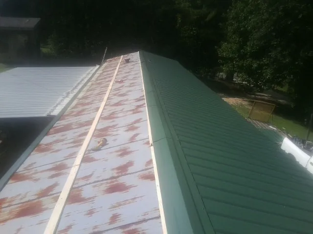 Old rusted panels beside newly installed green metal roofing — Wind Damage Roof Repair by Roofing Brothers in Eva