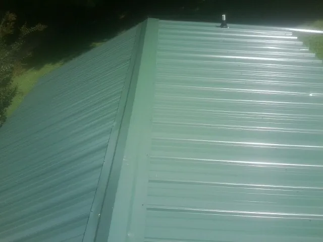 New green metal panels meeting at the ridge of a roof — Flat Roof Repair work by our crew in Eva