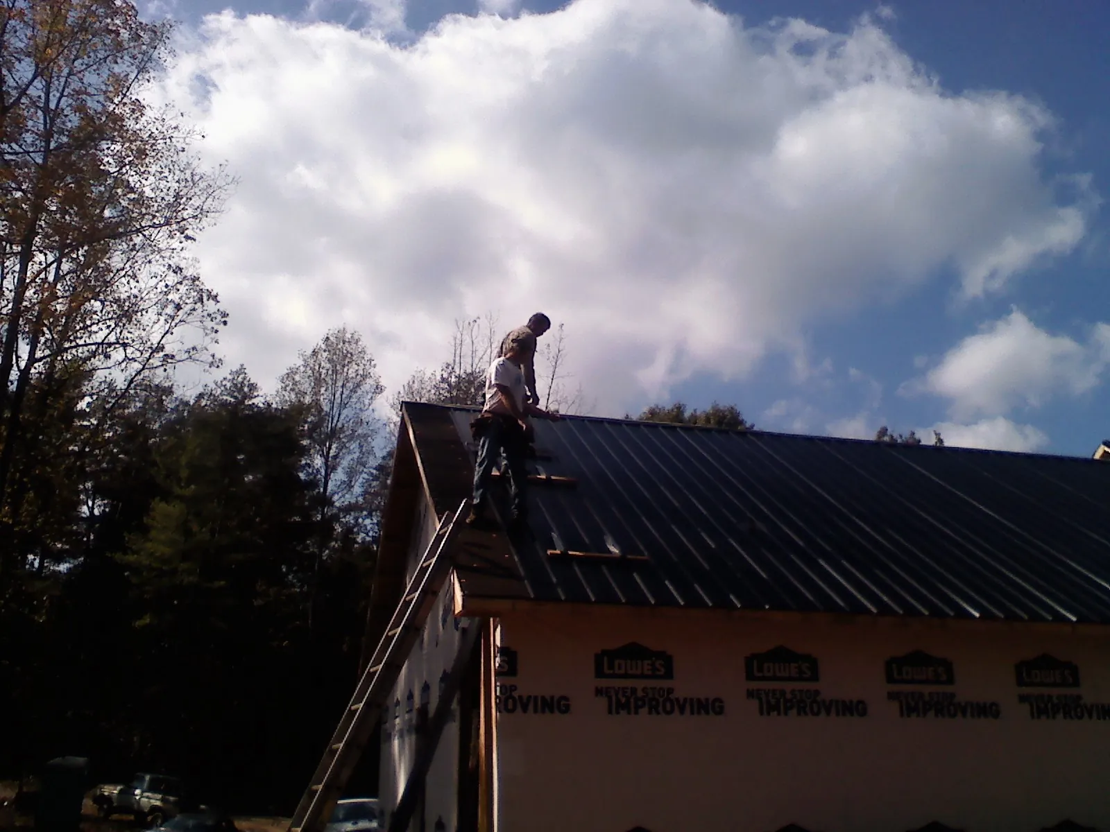Roofer fastening dark metal panels high against a cloudy sky, from a Roof Inspection job in Eva
