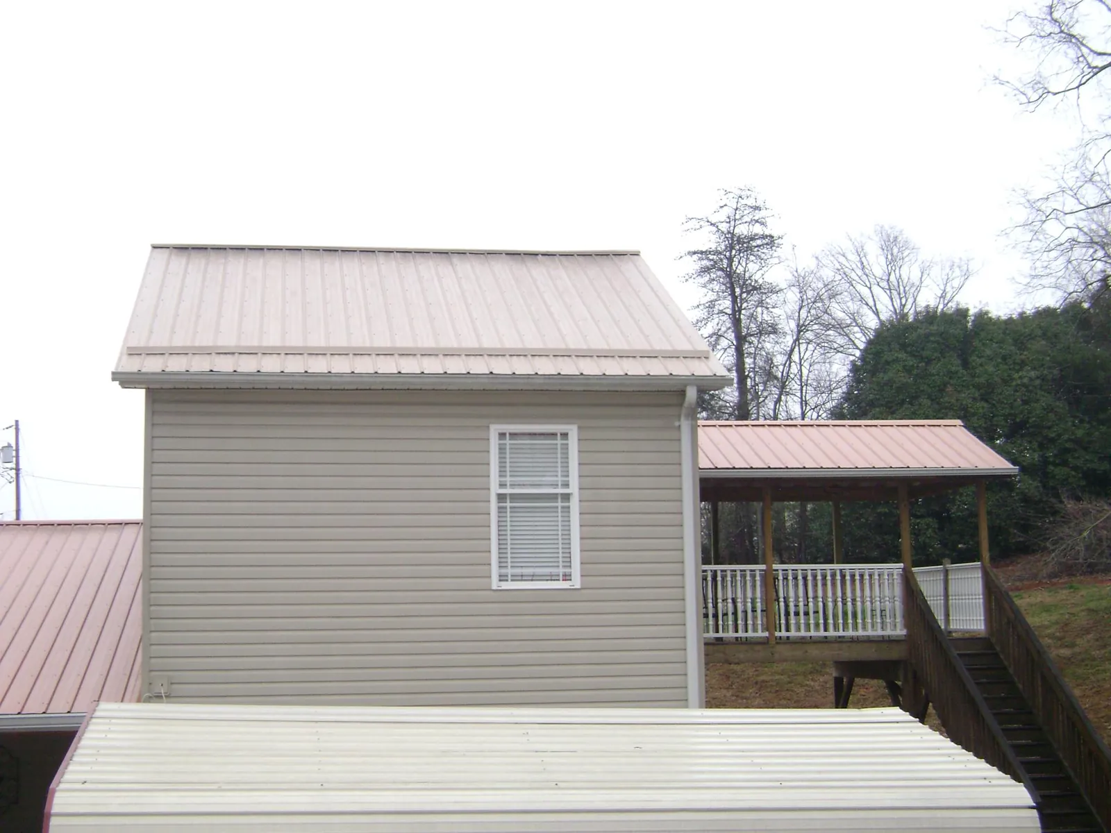 Tan metal roofs on a two story addition and attached porch, from a Roof Replacement job in Eva